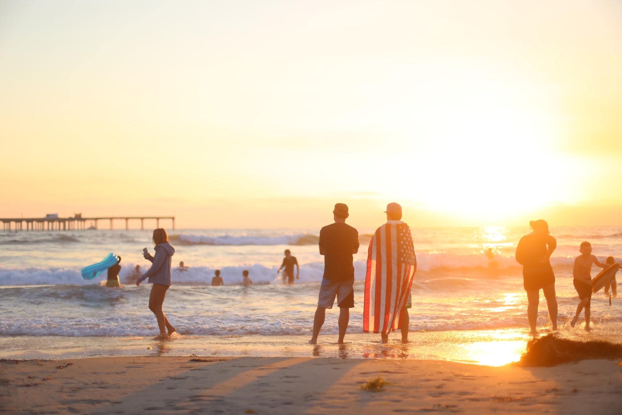 People at beach with person holding the flag of the united states during a sunset